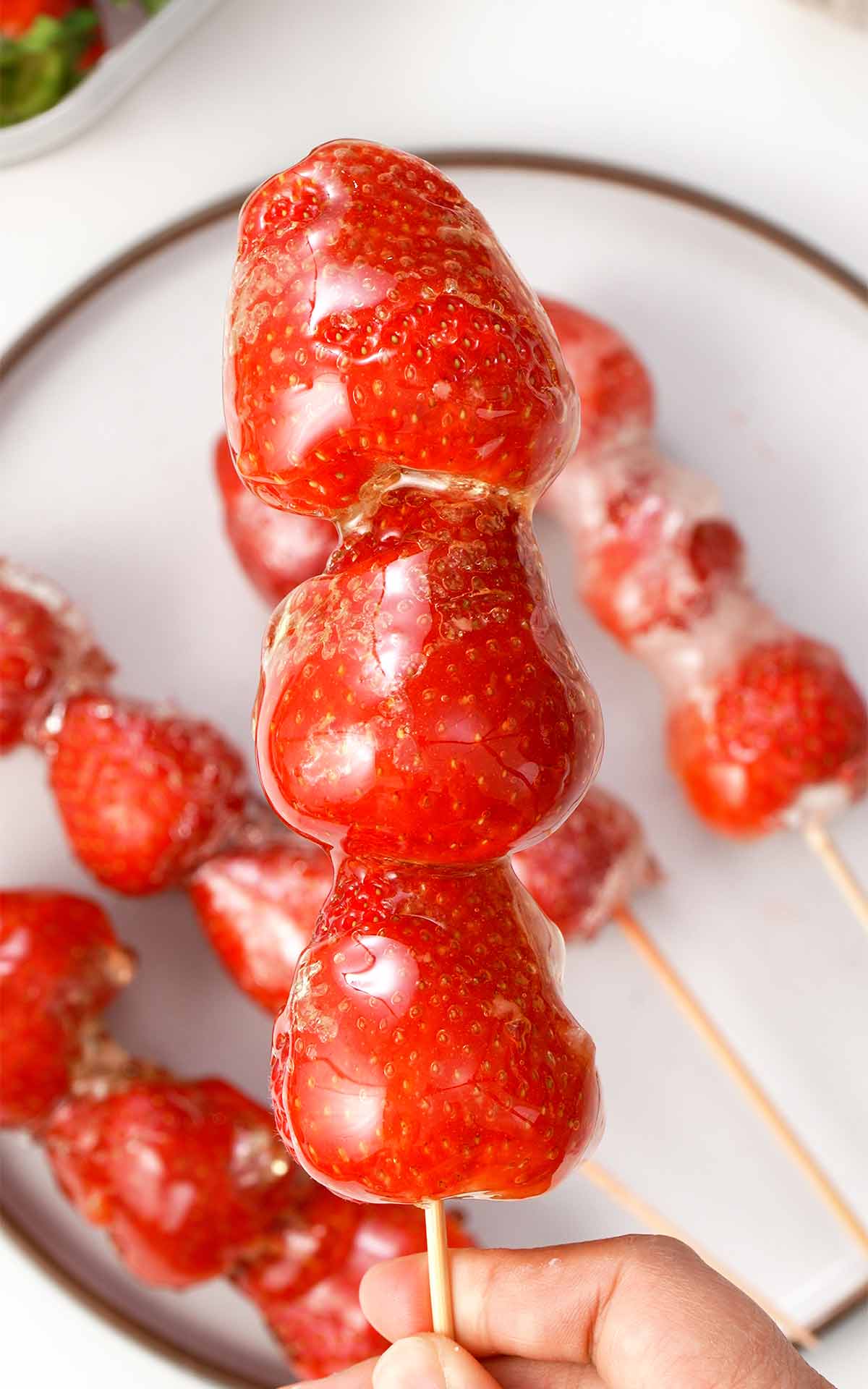 Glossy sugar coated vibrant red strawberry tanghulu on wooden skewers.