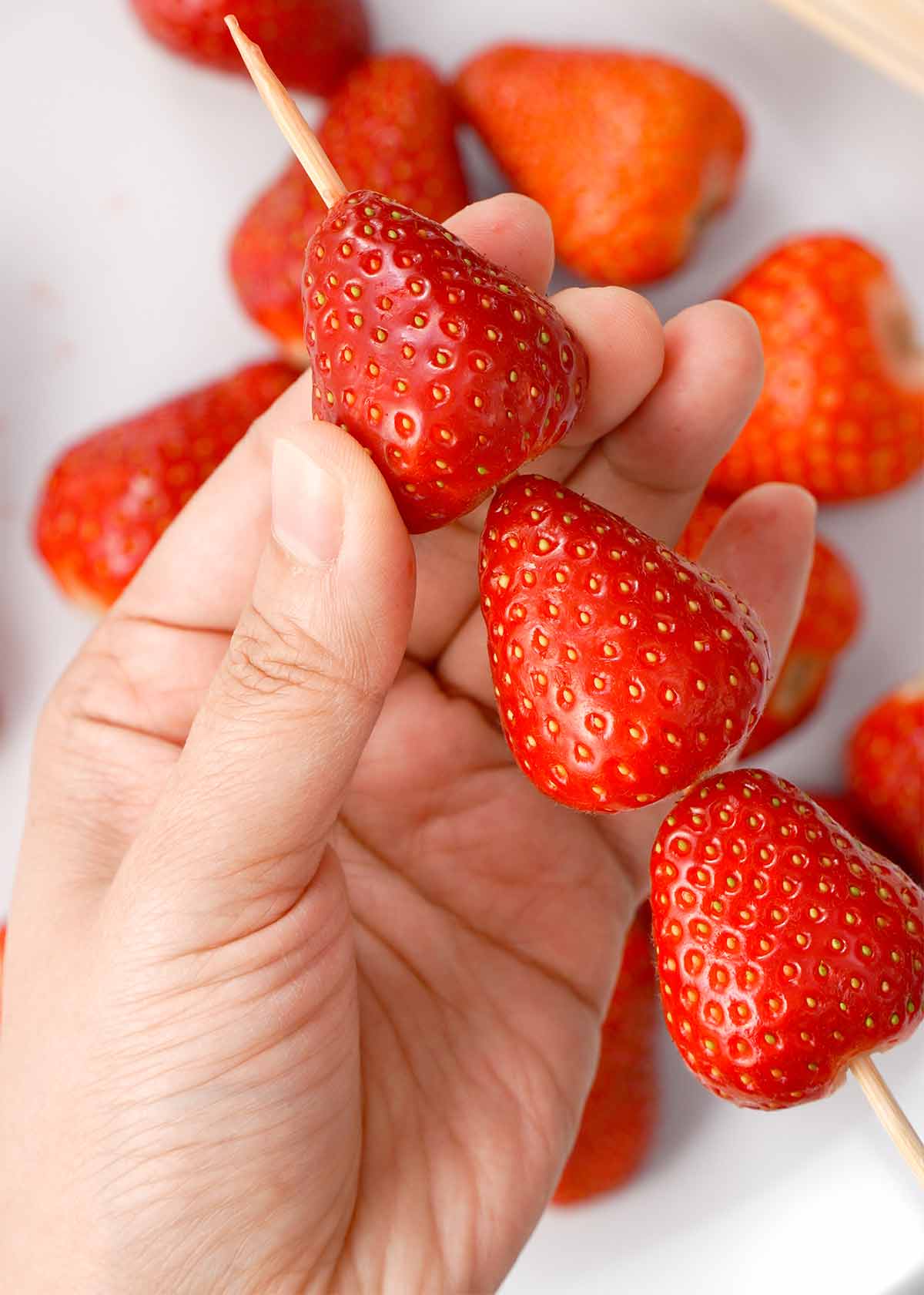 A photo of 3 red strawberry threaded on the wooden skewers. 