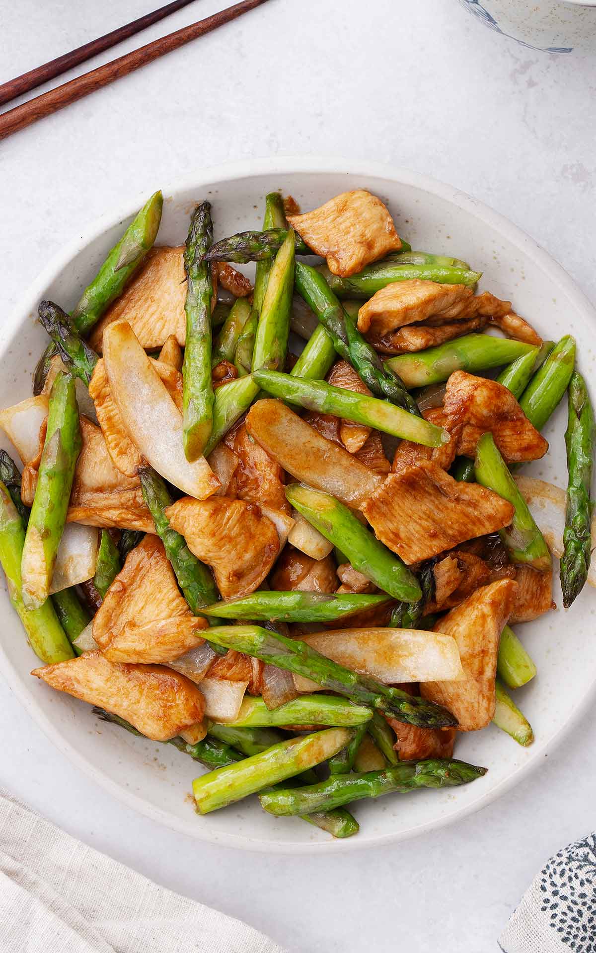 A white plate containing stir fried chicken and asparagus stir fry. 