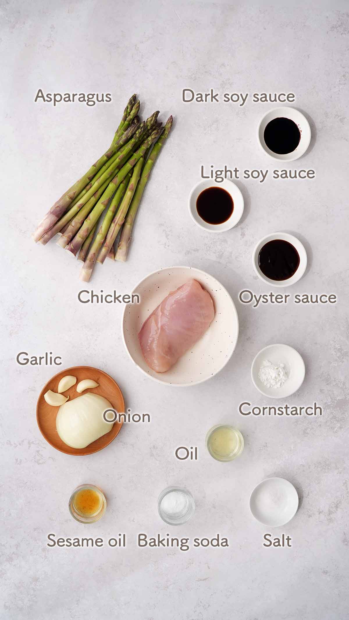 Labelled ingredients of making asparagus chicken recipe, displayed on the white table. 