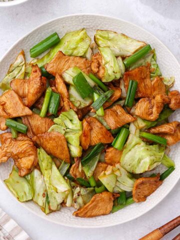 A white plate containing chicken and cabbage stir fry with green onions.