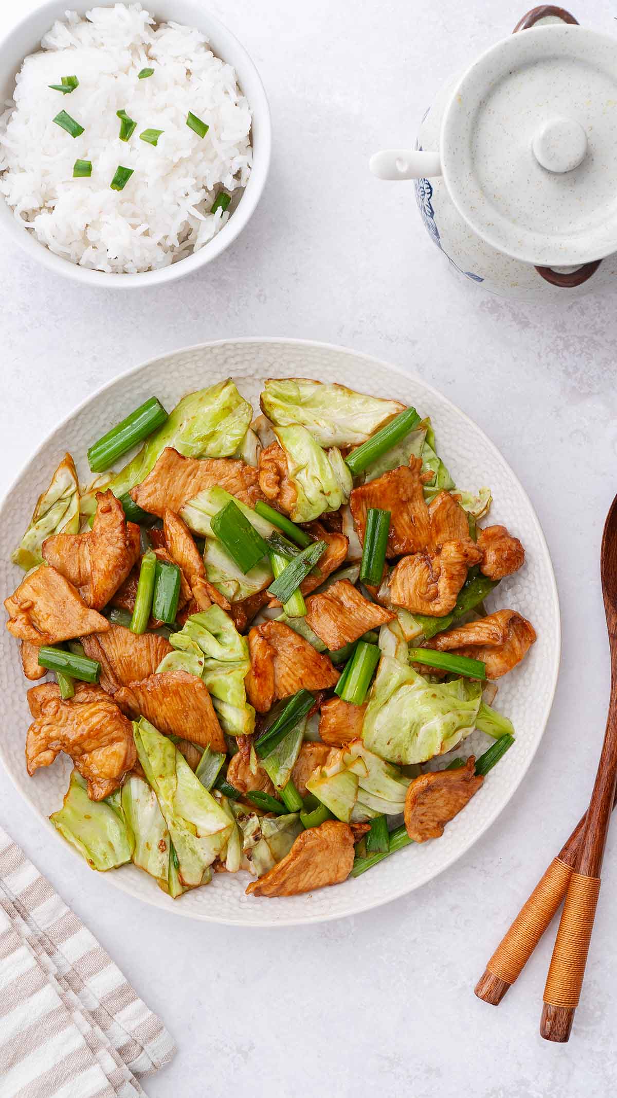 A white plate containing stir fried chicken slices and cabbage with rice on the side. 