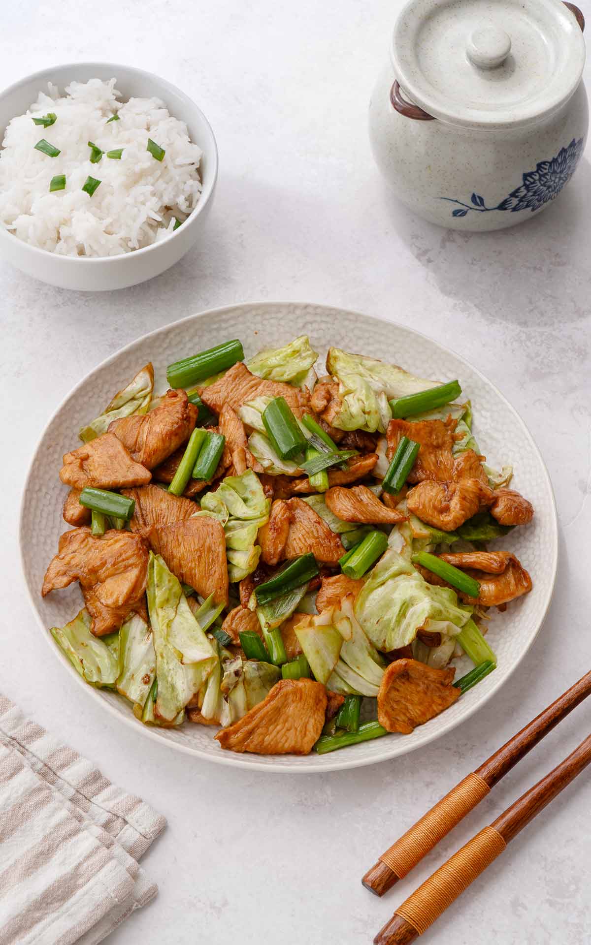 A white serving plate containing, stir fried chicken slices and cabbage and spring onions.