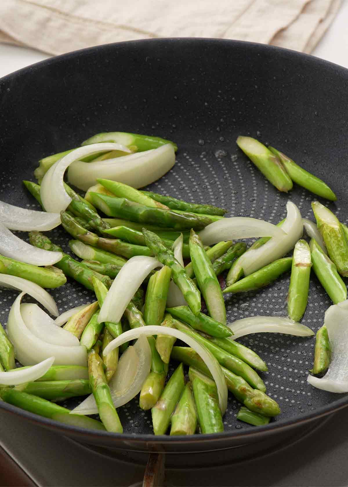 An image of a black wok containing stir fried asparagus and onions. 