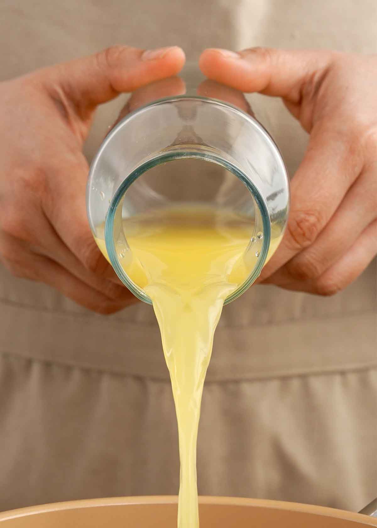 An image of a pair of hands pouring the yellow colour juice into the pot.