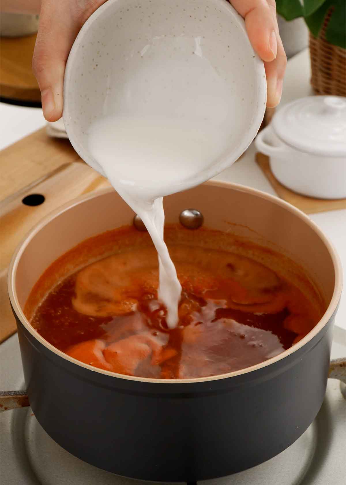 A picture of pouring the white colour cornstarch water into the sauce pot.