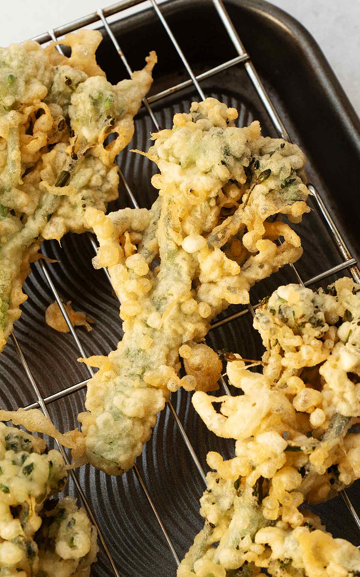 Fried golden broccoli tempura florets displayed on the cooling rack.