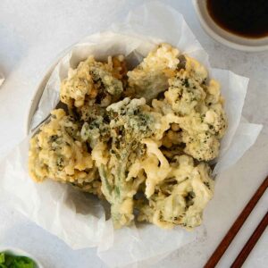 A white bowl containing fried tempura broccoli bites.