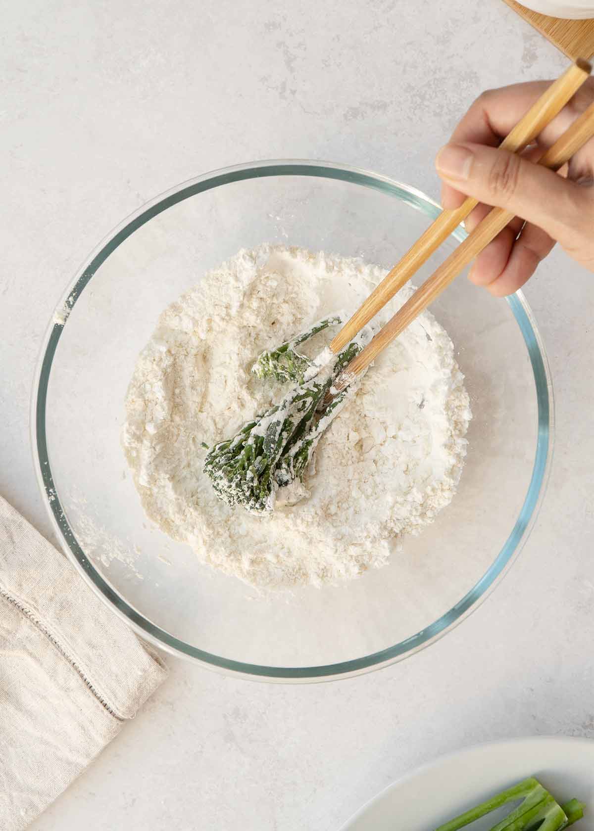 An image showing how to dredge broccoli pieces in the tempura flour mix.