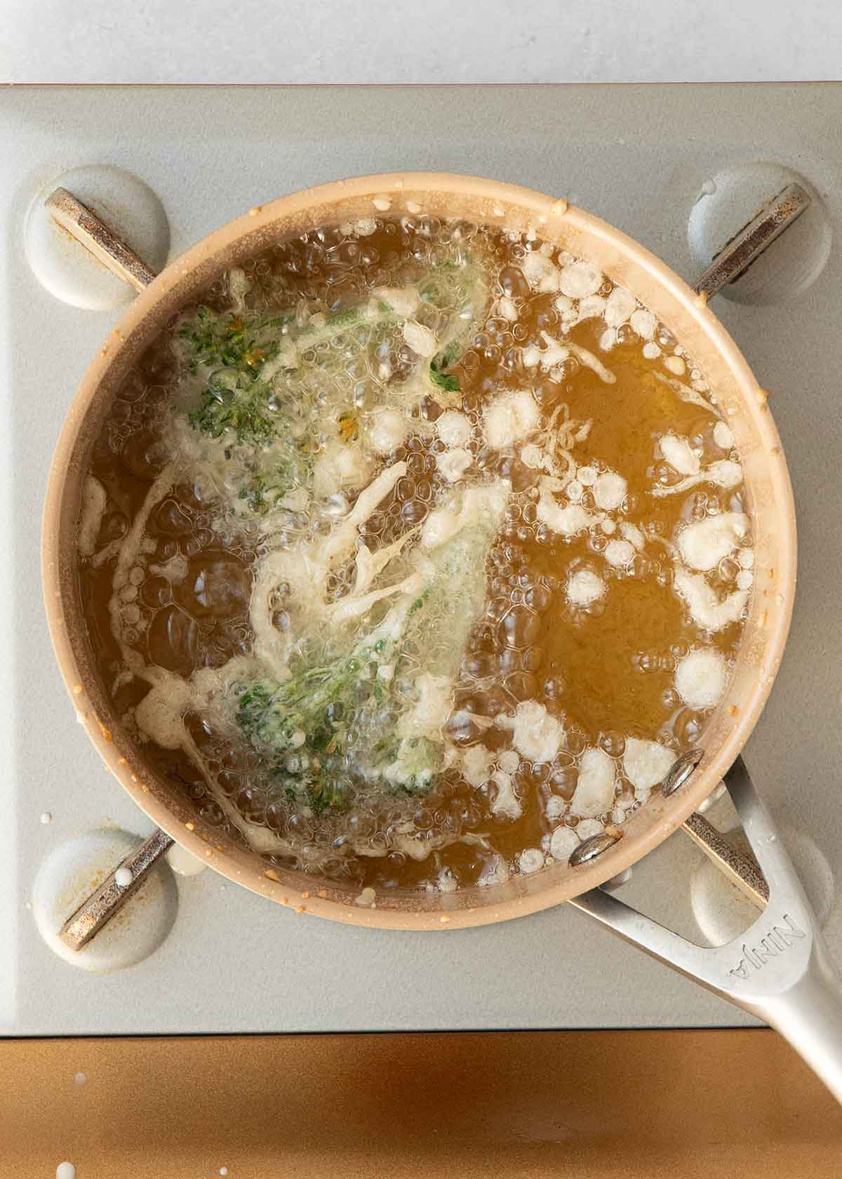 An image of frying tempura battered broccoli florets in the oil.