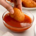 A picture of a fried chicken piece dipped in the red colour sweet and sour sauce dipping sauce.