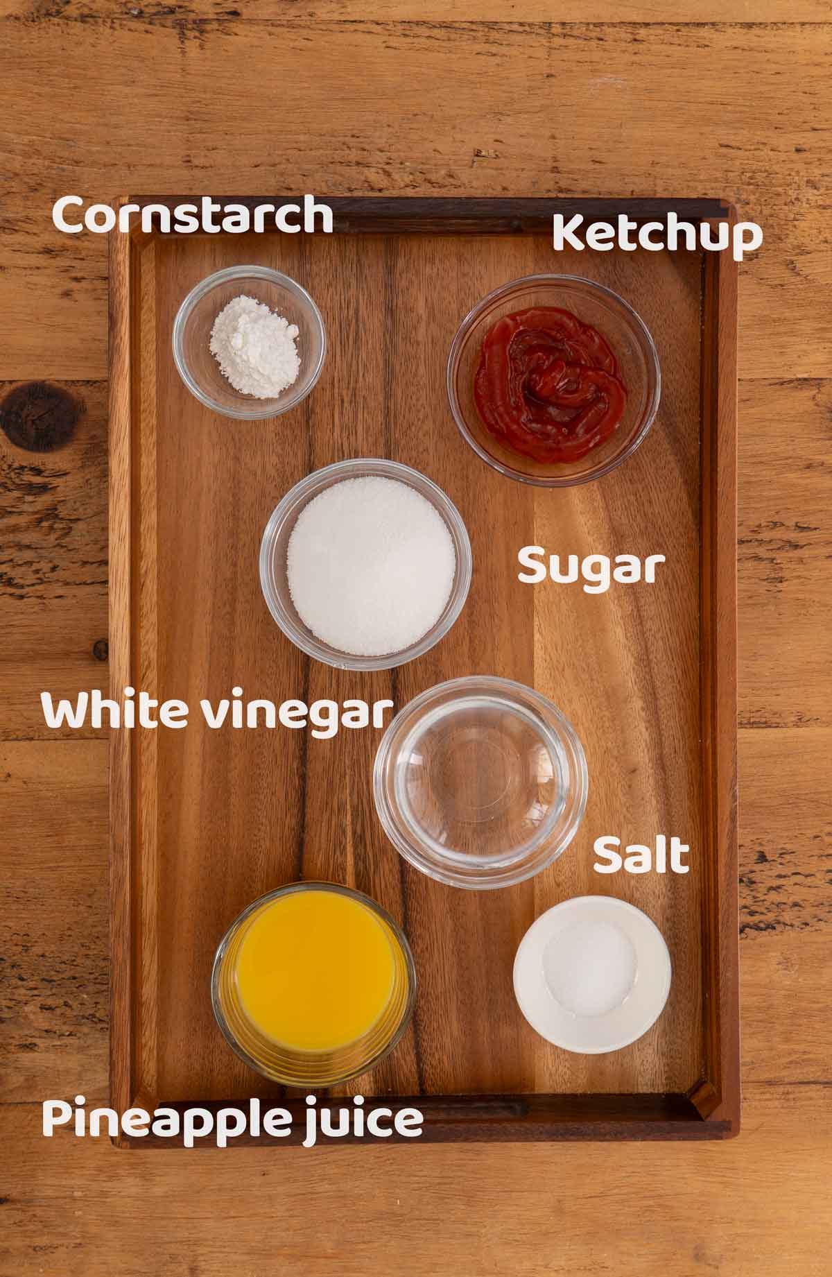 Labelled ingredients of making sweet and sour sauce displayed on the wooden tray.