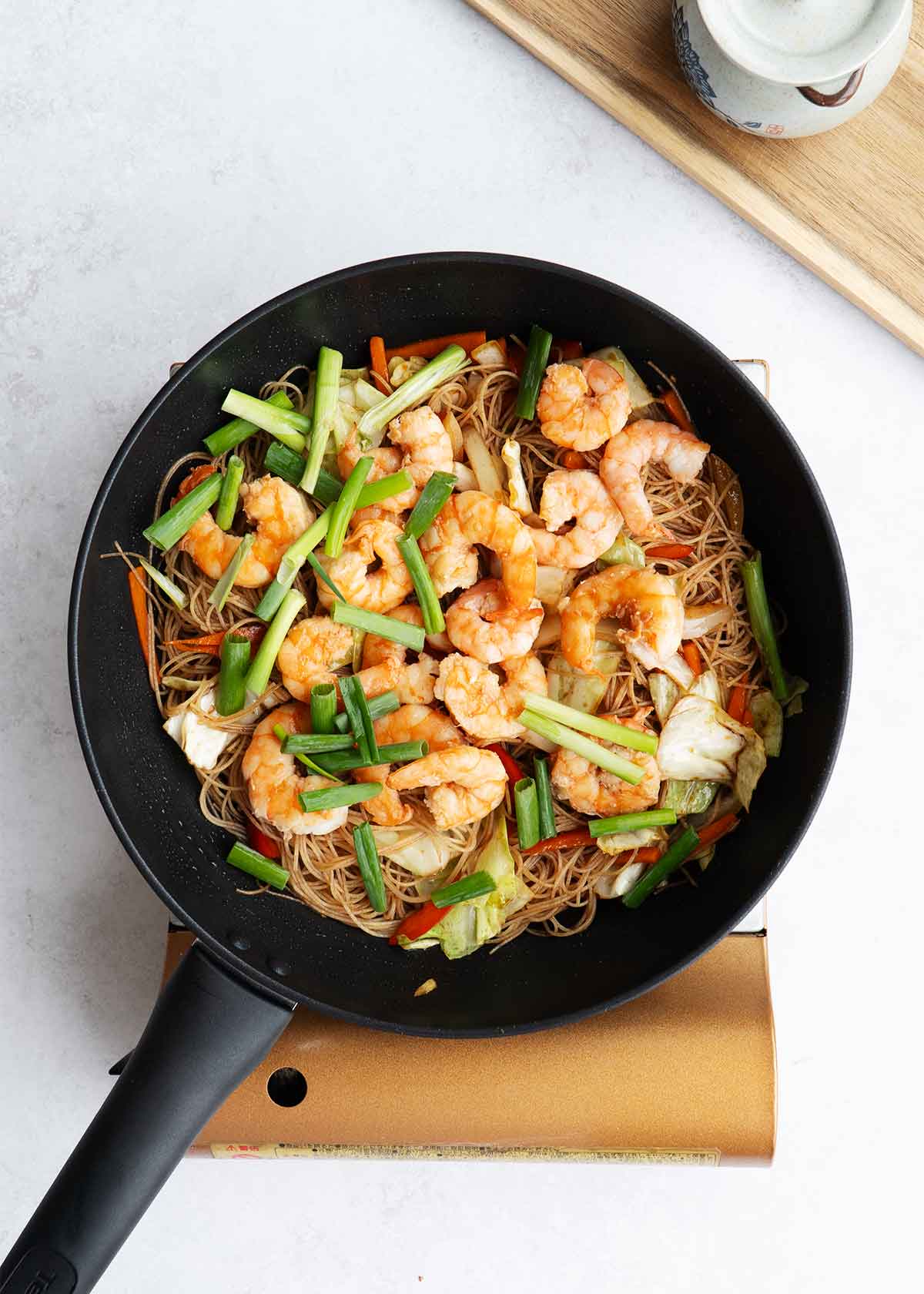 A black wok containing, rice vermicelli, shrimp, and mixed colourful vegetables.