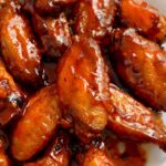 An image of fried chicken wings glazed with glossy red hot and honey sauce.