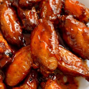 An image of fried chicken wings glazed with glossy red hot and honey sauce.