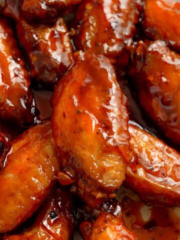An image of fried chicken wings glazed with glossy red hot and honey sauce.