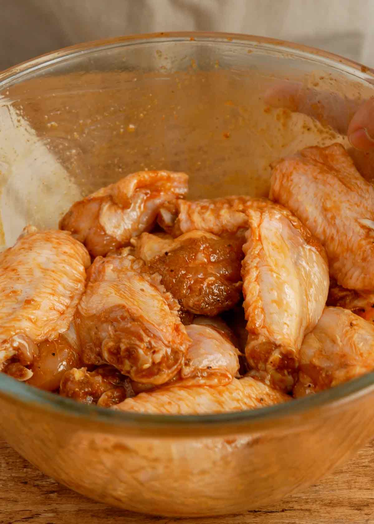 A transparent mixing bowl containing marinated chicken wings.