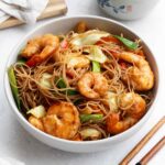 A white bowl containing mei fun noodles with shrimp, cabbage, carrot, and colourful vegetables.