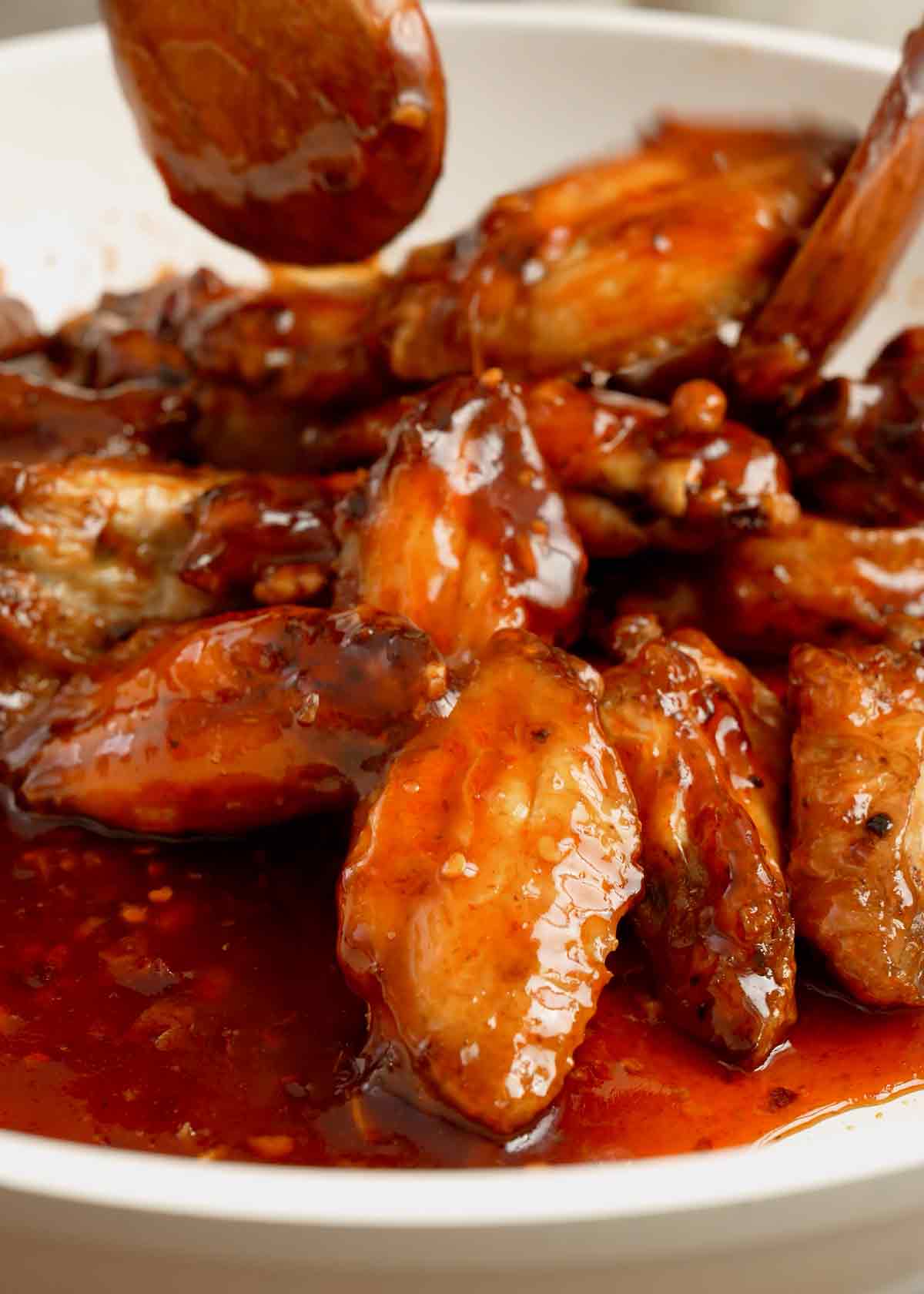 A white pan containing fried chicken wings with glossy red colour honey hot sauce.