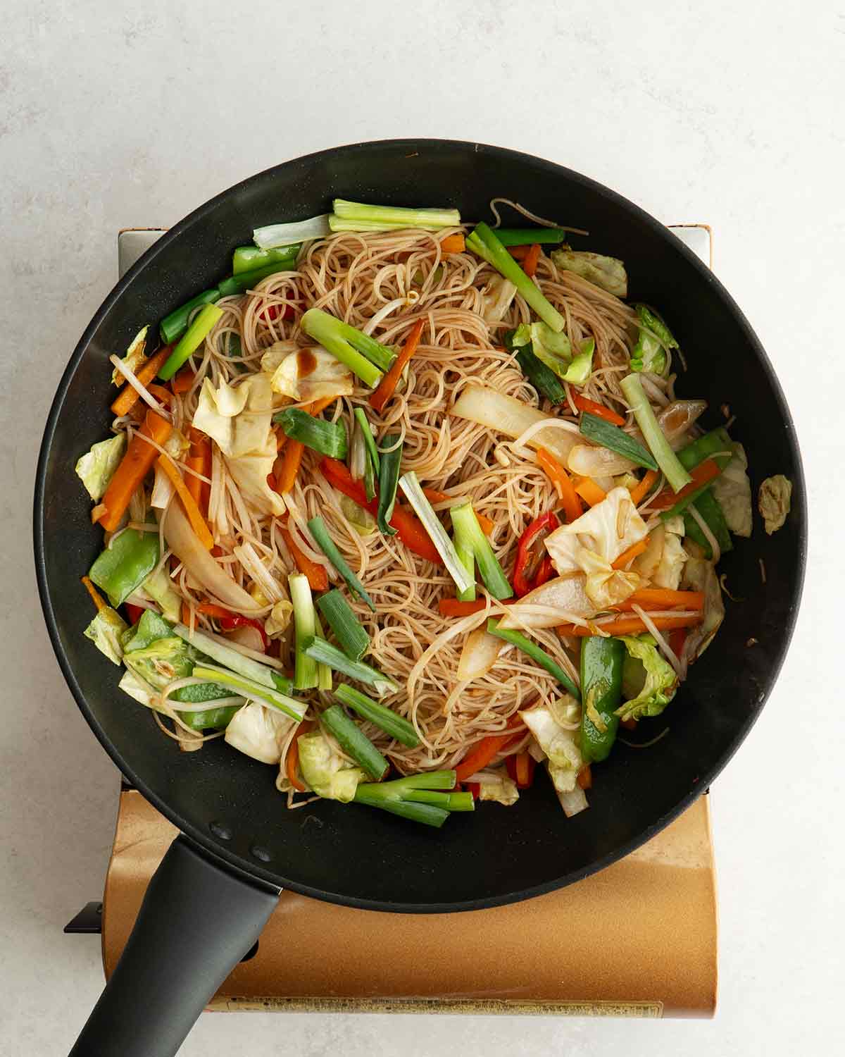 An image of stir fried mixed vegetables and rice vermicelli in a large wok.