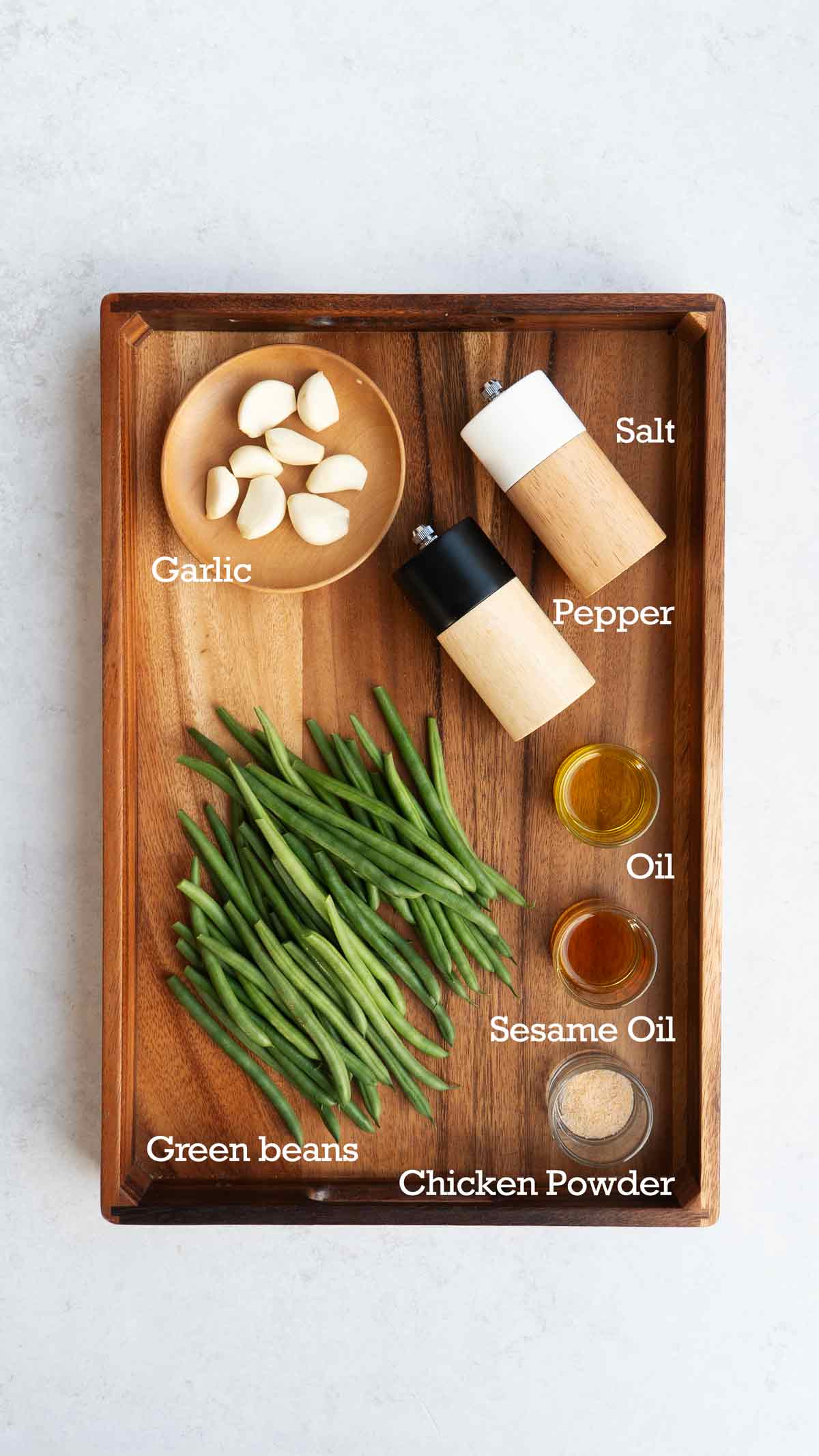 Labelled ingredients of making green beans stir fry displayed on the wooden tray.