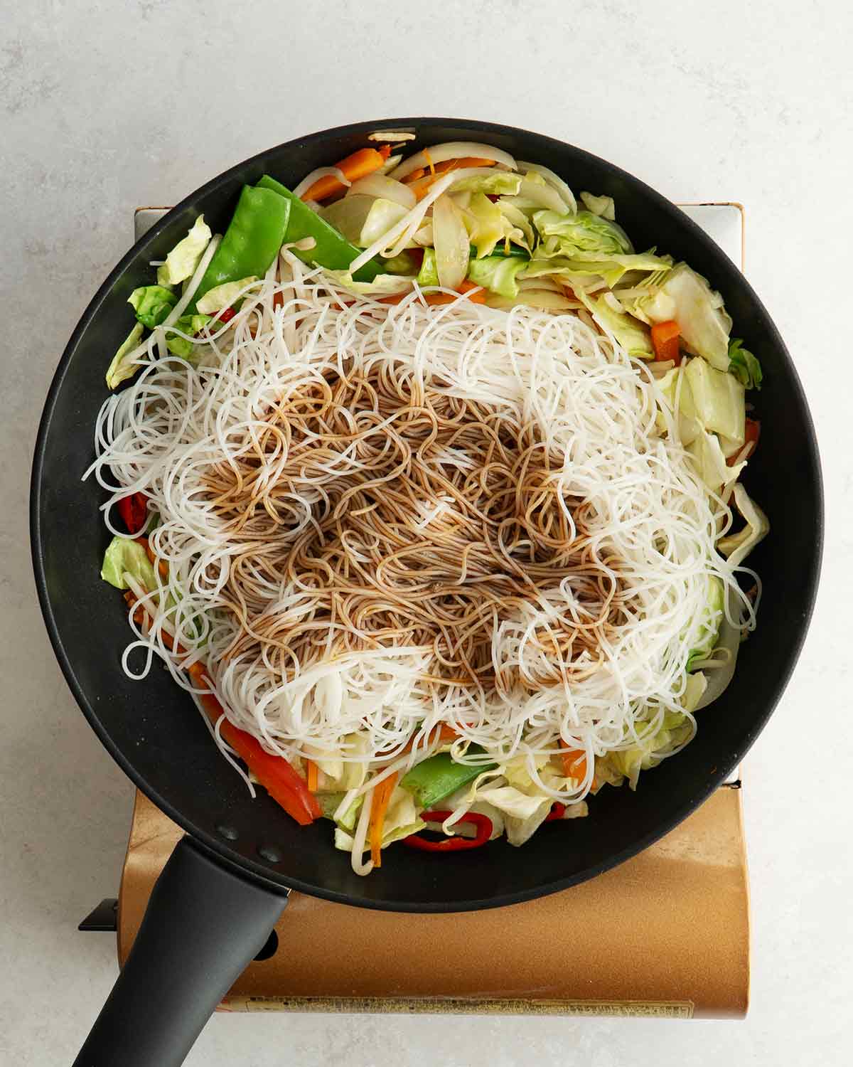 An image showing adding mei fun noodles and sauce to the wok.