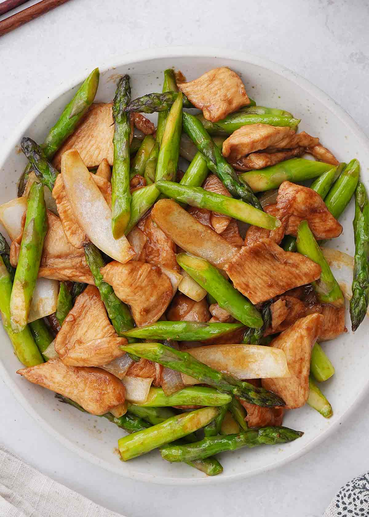 Stir fried chicken slices with asparagus displayed on the white plate.