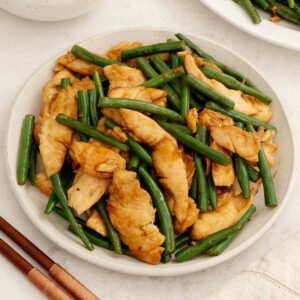 A white plate containing stir fry chicken with green beans.