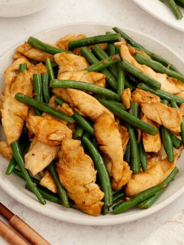 A white plate containing stir fry chicken with green beans.