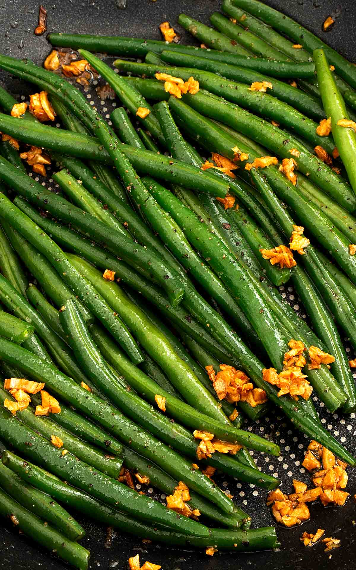 A black wok containing stir fried vibrant green colour beans and golden fried garlic.