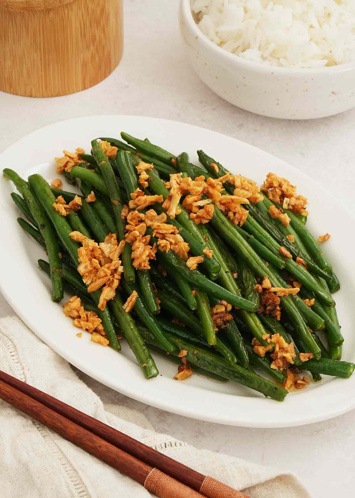 Stir fry green beans and golden fried garlic displayed on the white plate.