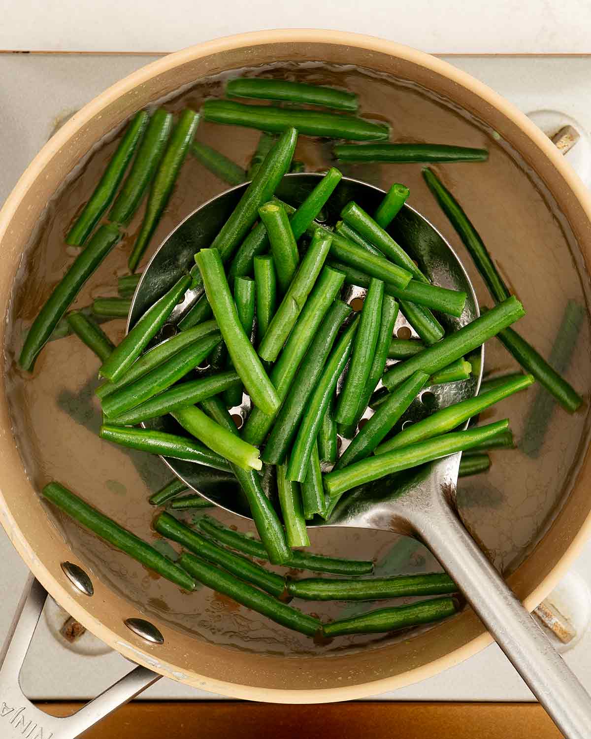 An image showing how to blanch green beans in boiling water in a saucepan.