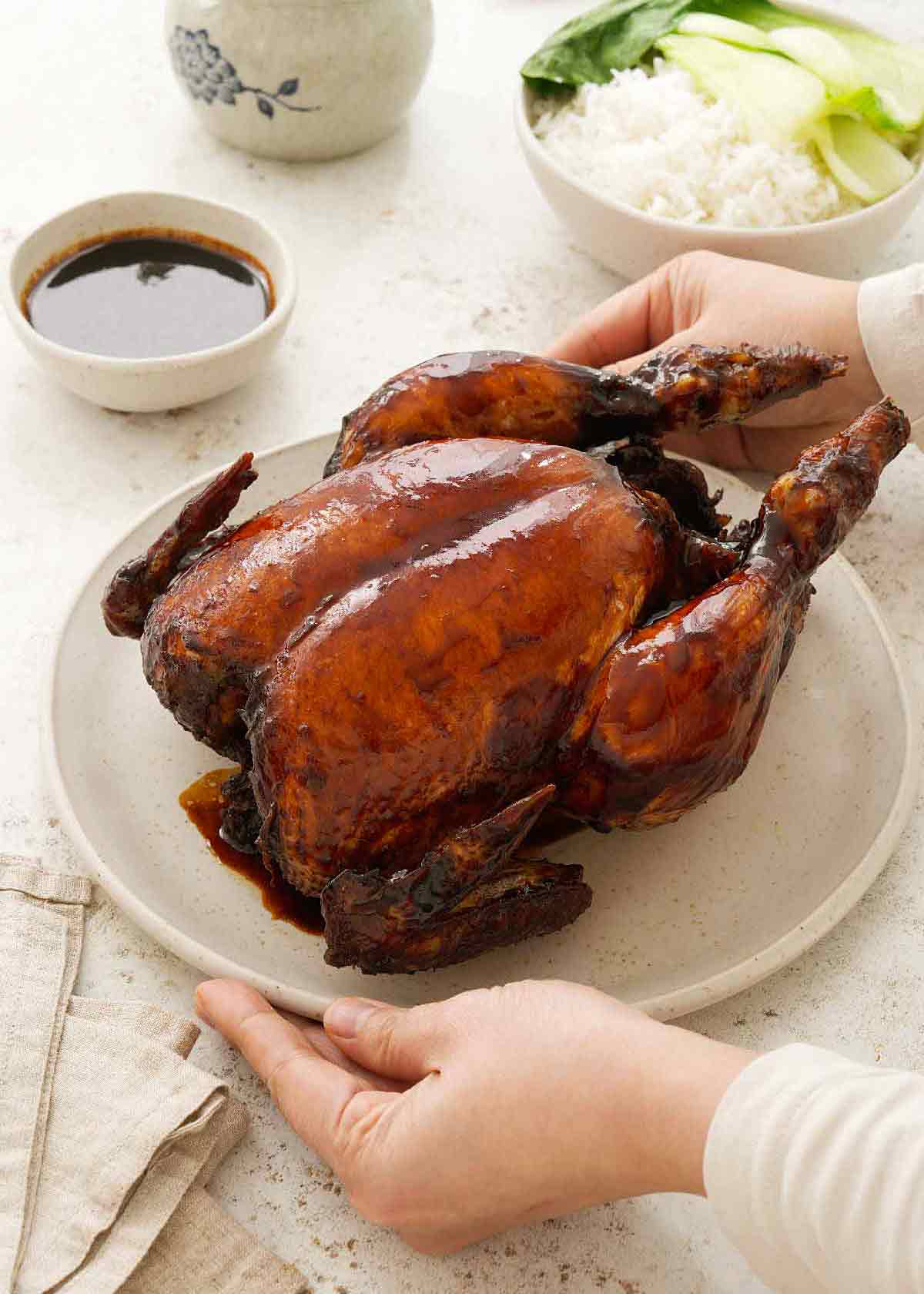 Glossy soy sauce braised whole chicken displayed on the white plate.