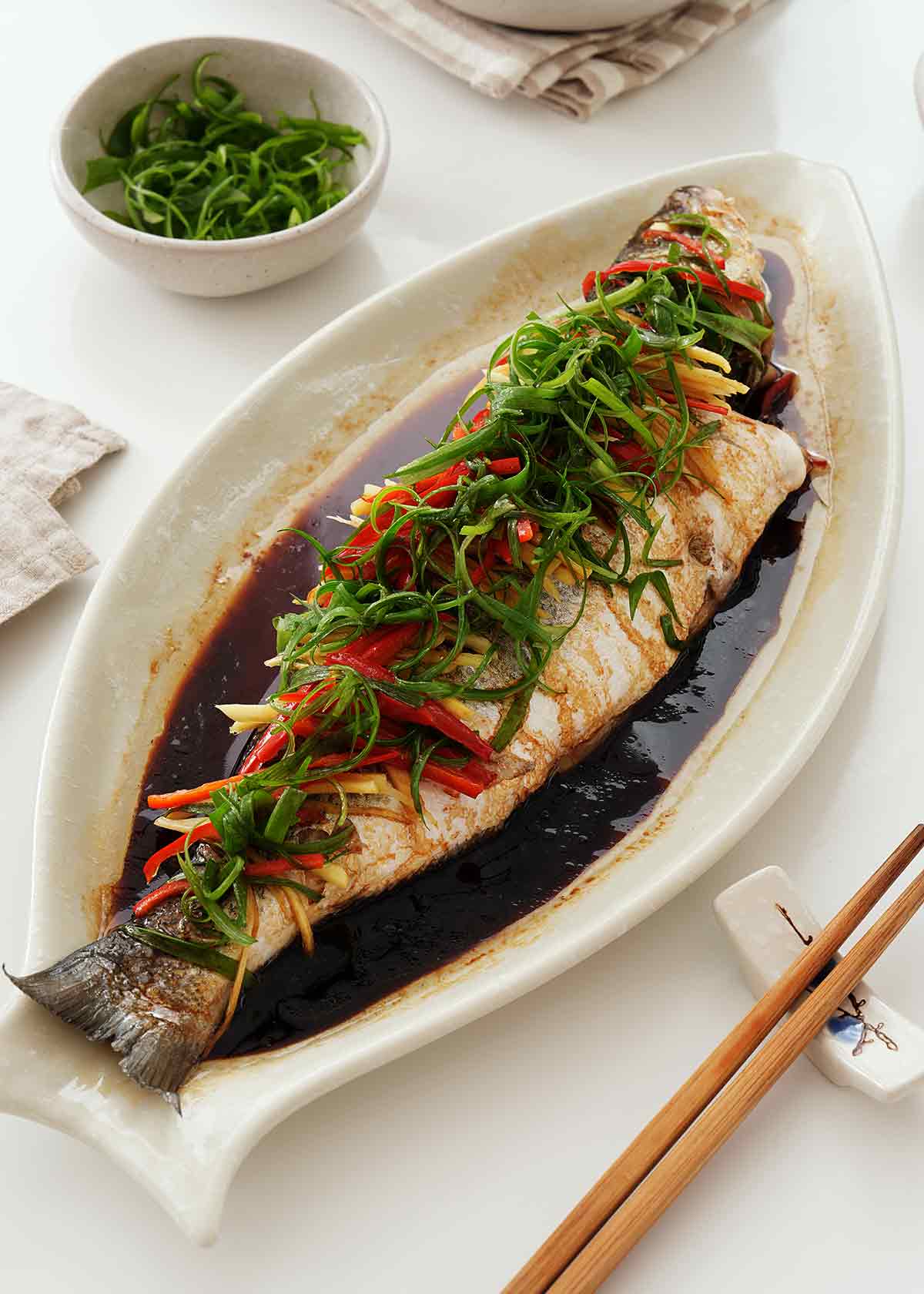 Steamed whole sea bass topped spring onions and chilli strips on top with soy sauce on the sauce.