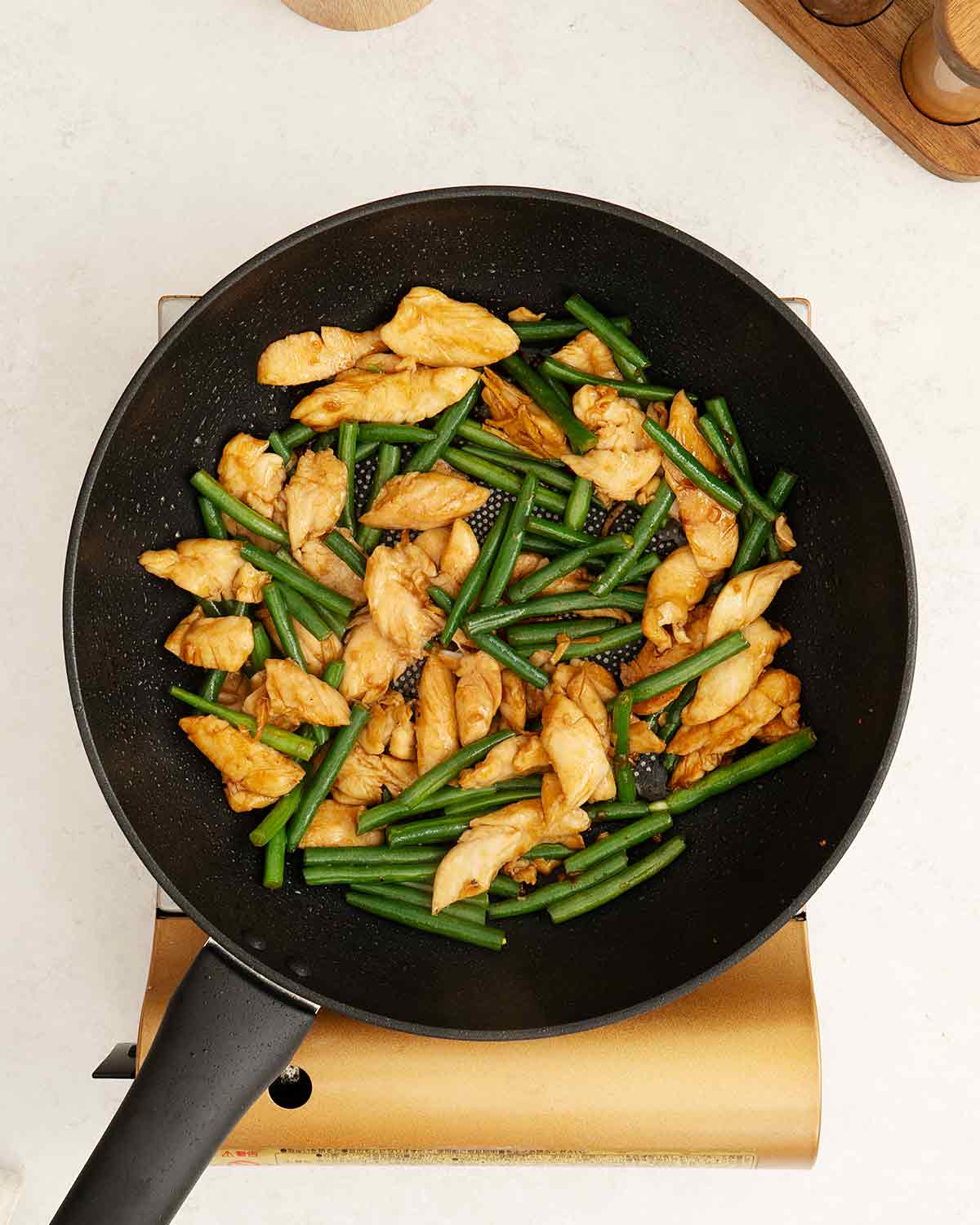 A large wok containing stir fried green beans and chicken slices.
