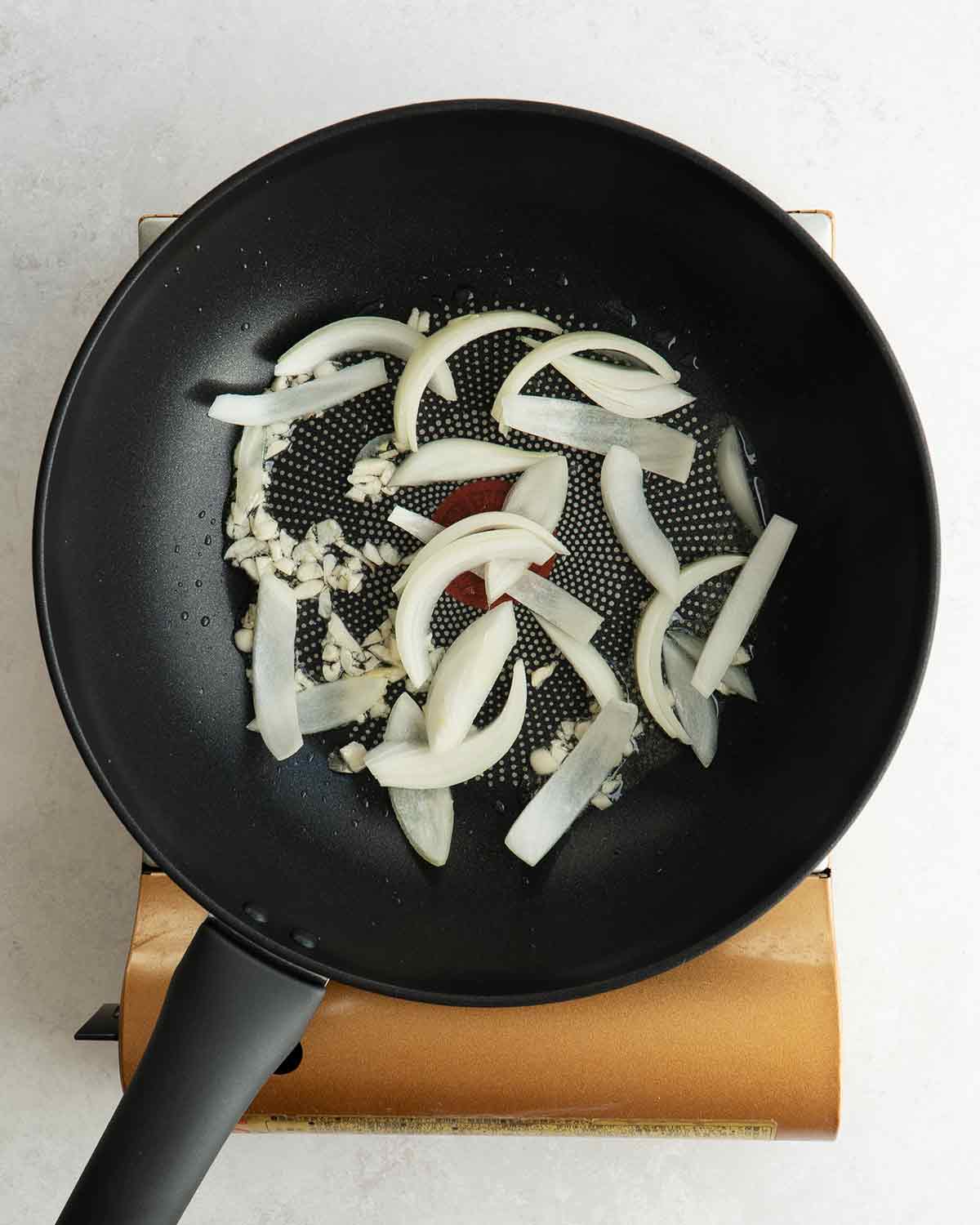 A black wok containing stir fried garlic and onions.