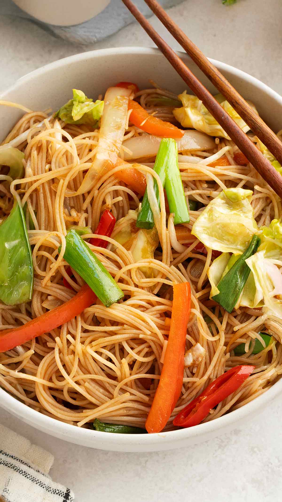 A white bowl containing stir fried mei fun noodles with colourful vegetables. 