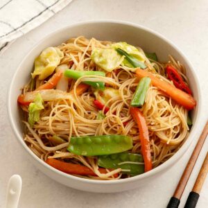 A white bowl containing fried mixed colourful vegetables and mei fun noodles.