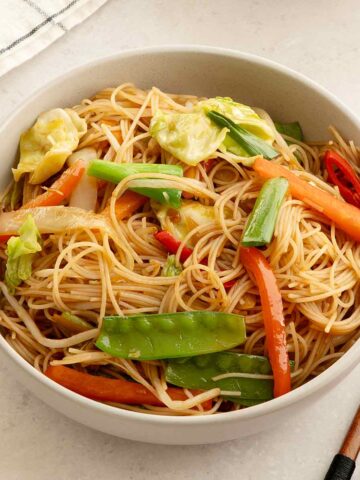 A white bowl containing fried mixed colourful vegetables and mei fun noodles.