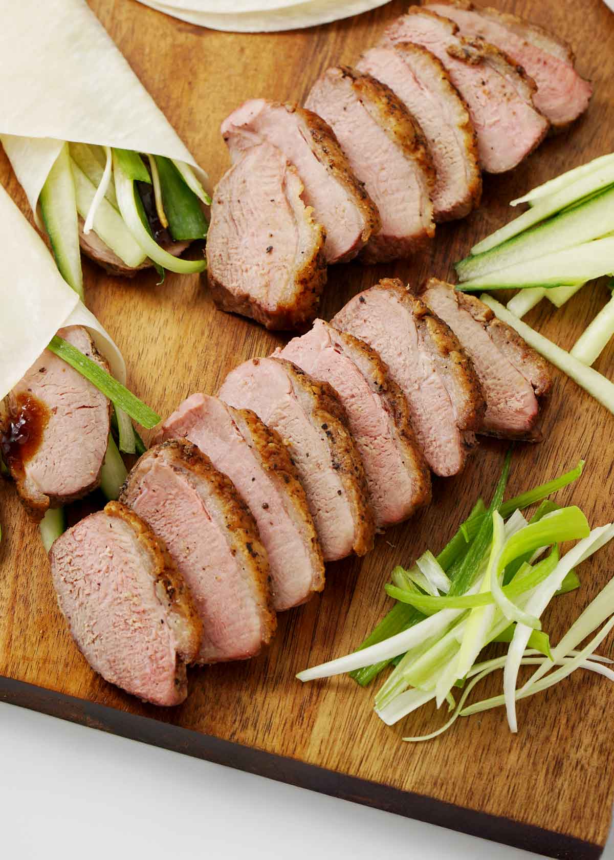 Roasted duck slices with hoisin sauce and pancake rolls displayed on the wooden tray.