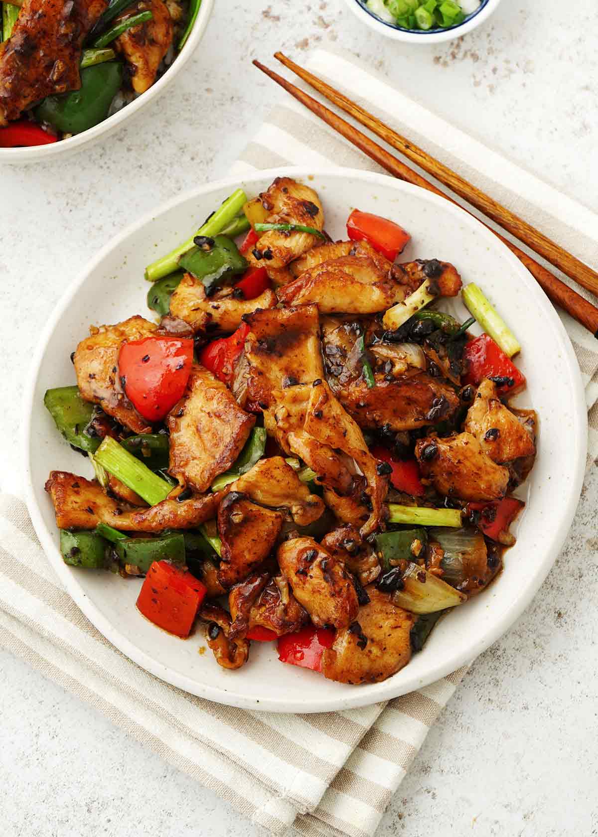A white plate containing chicken and mix vegetables with black bean sauce.