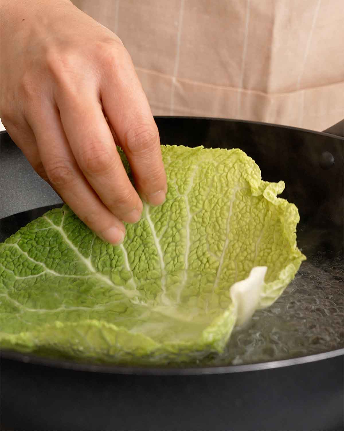 An image showing how to blanch green cabbage leaves in hot water.