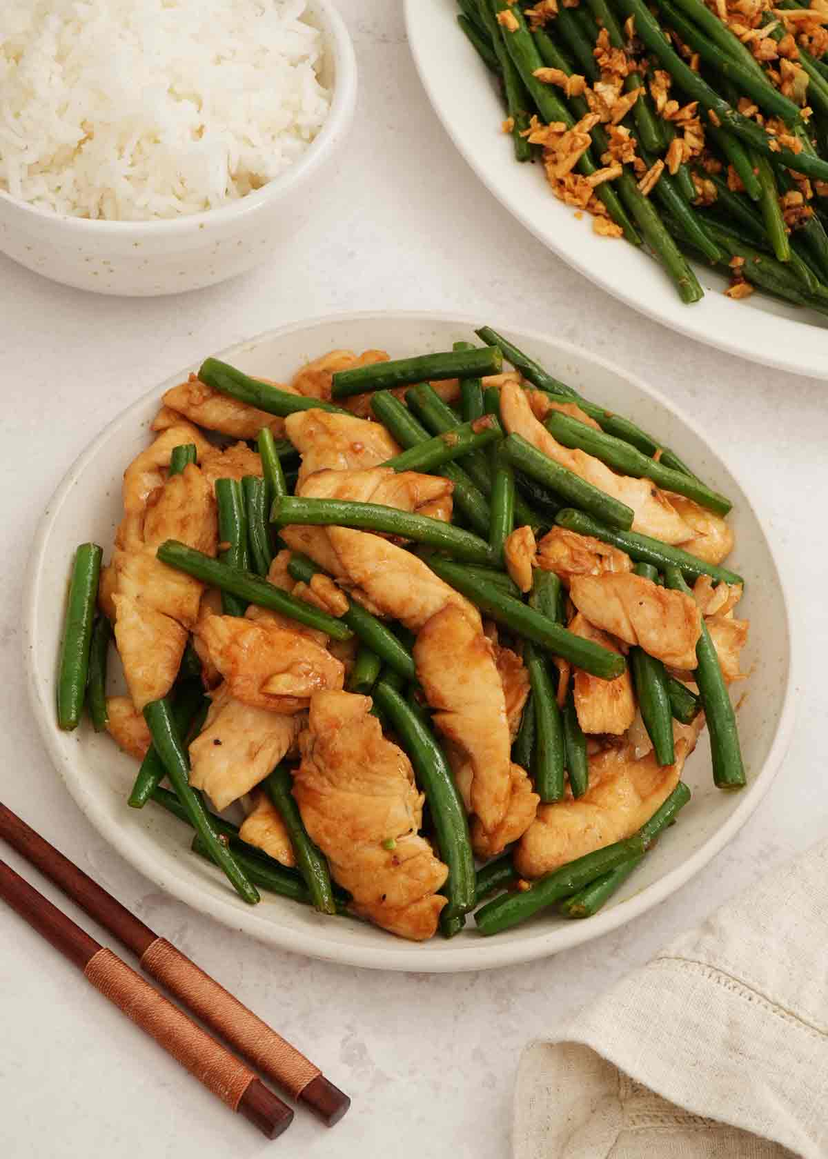 A white plate containing chicken slices with green beans.