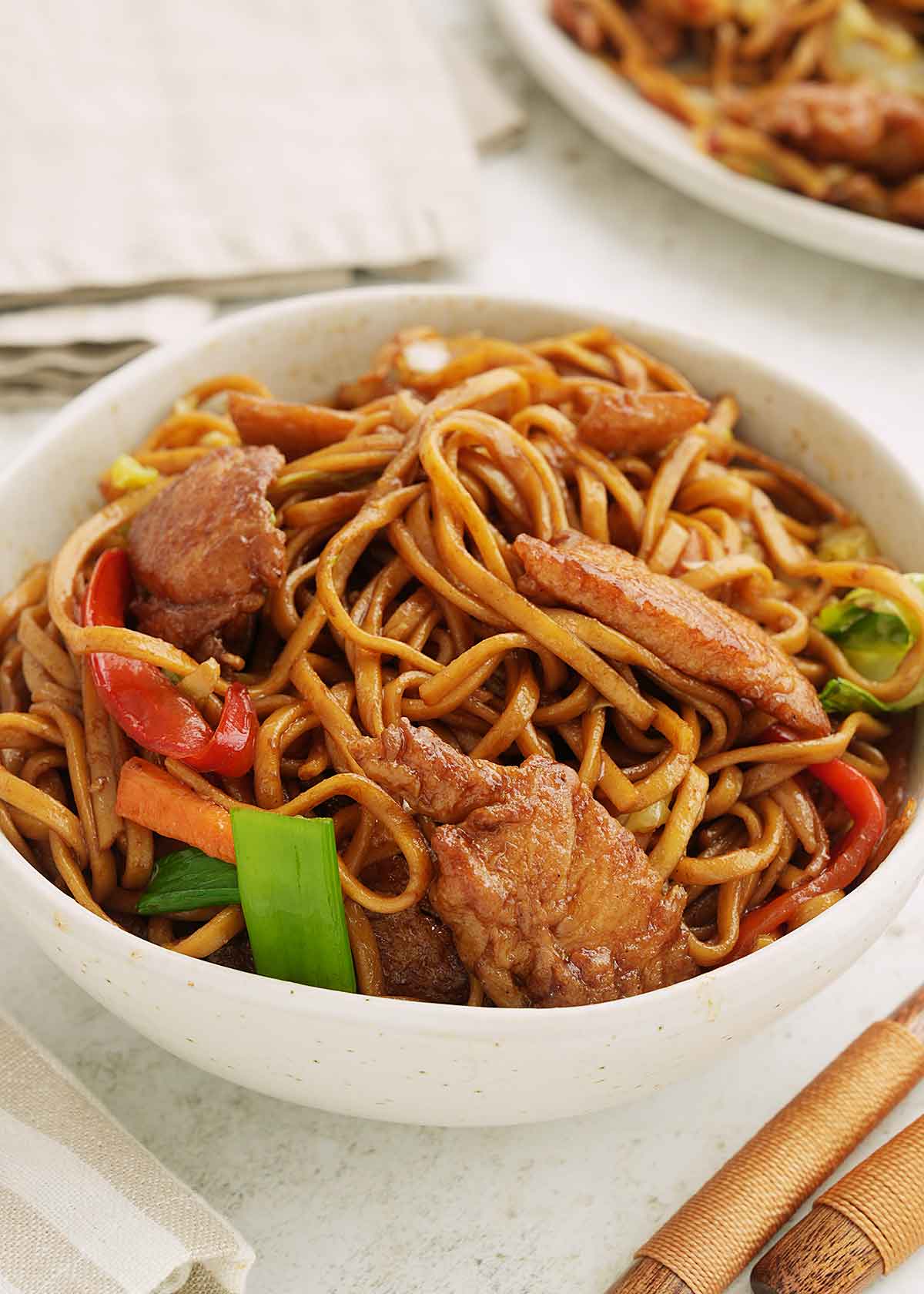 A white bowl containing chow mein with chicken and colourful mix vegetables.