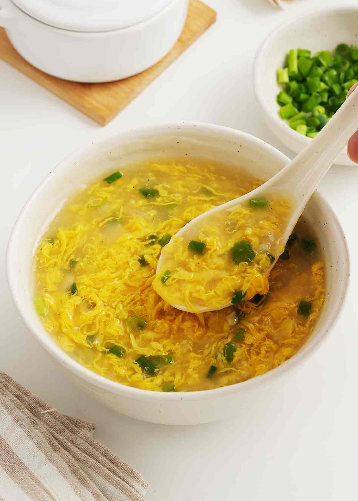 A small bowl containing yellow colour egg drop soup with chopped green onions.
