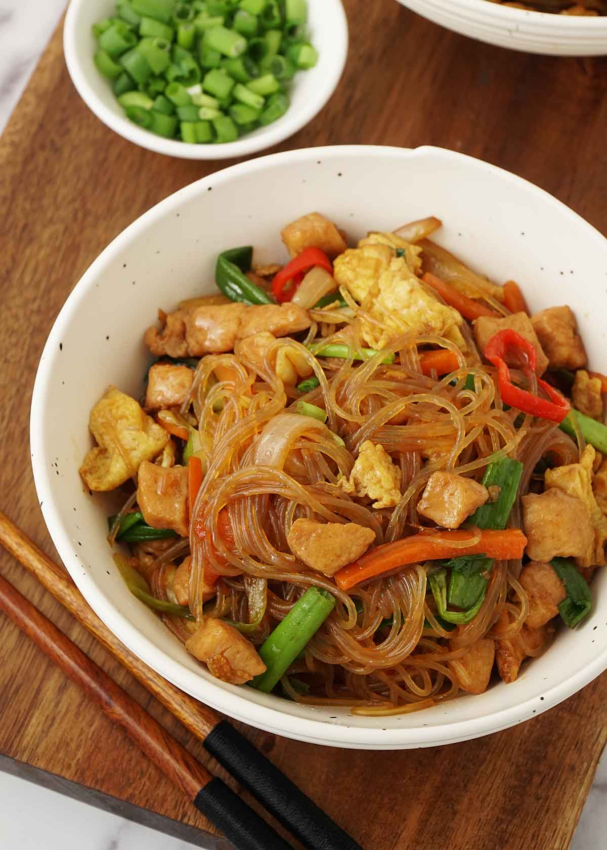 An image of a white bowl containing glass noodles, scrambled egg, and mixed vegetables.