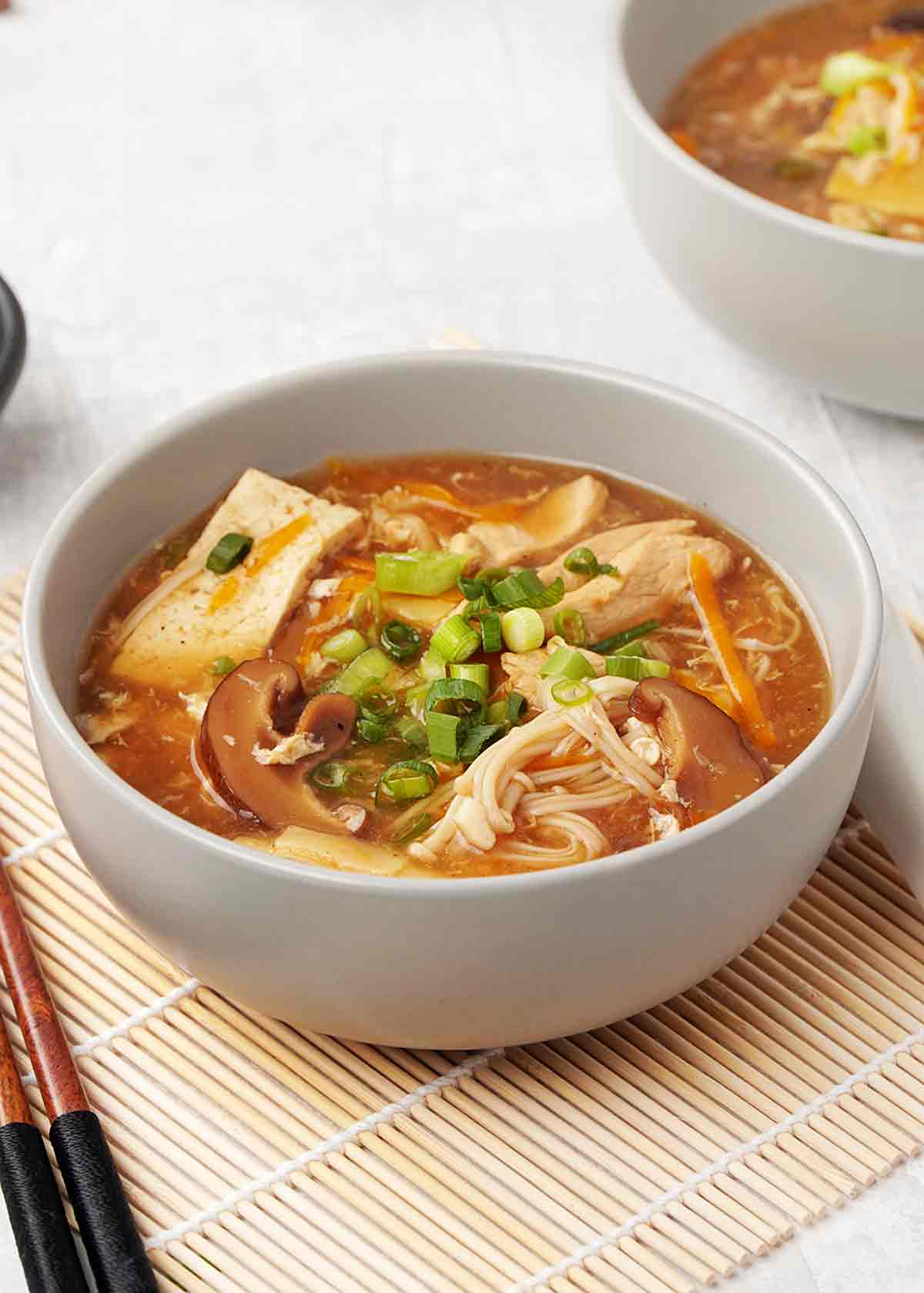 A grey bowl containing hot and sour soup with tofu, mushrooms and green onions garnish.