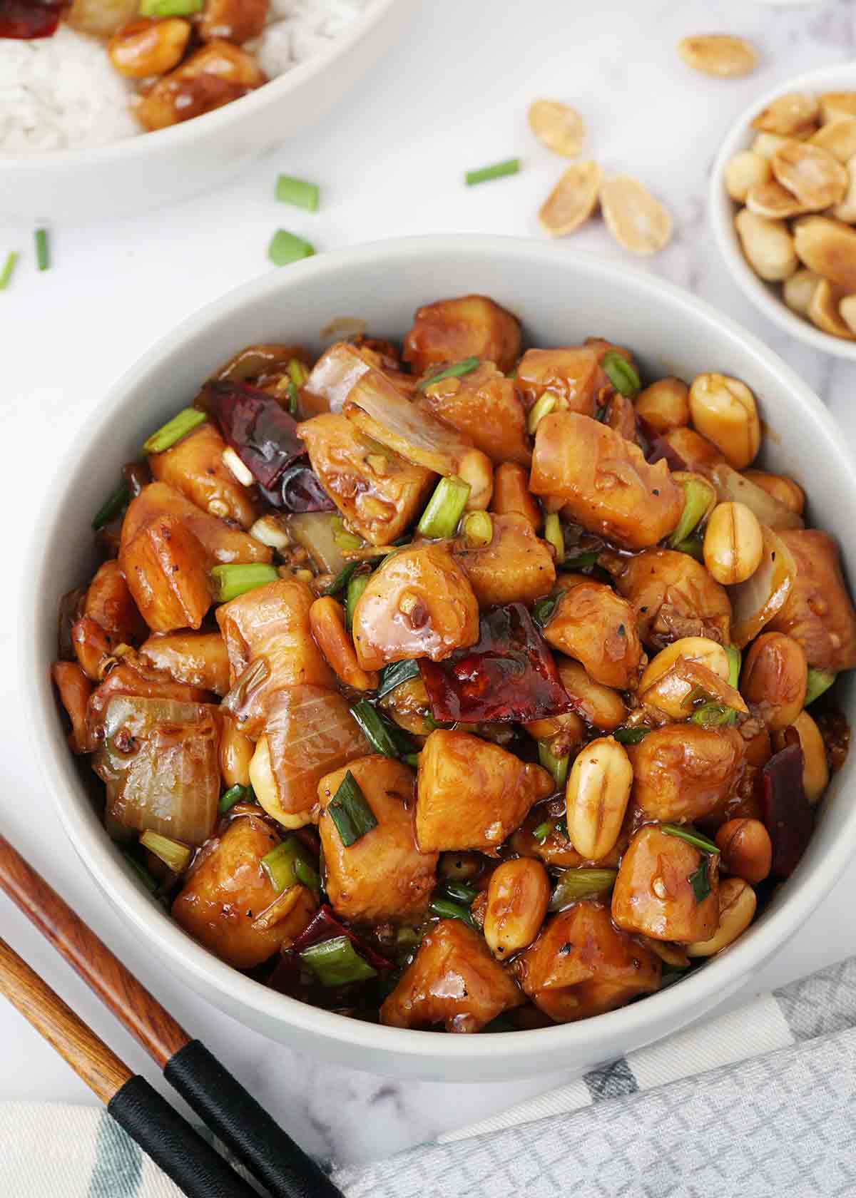 A grey bowl containing kung pao chicken stir fry with peanuts and dried chilli slices.