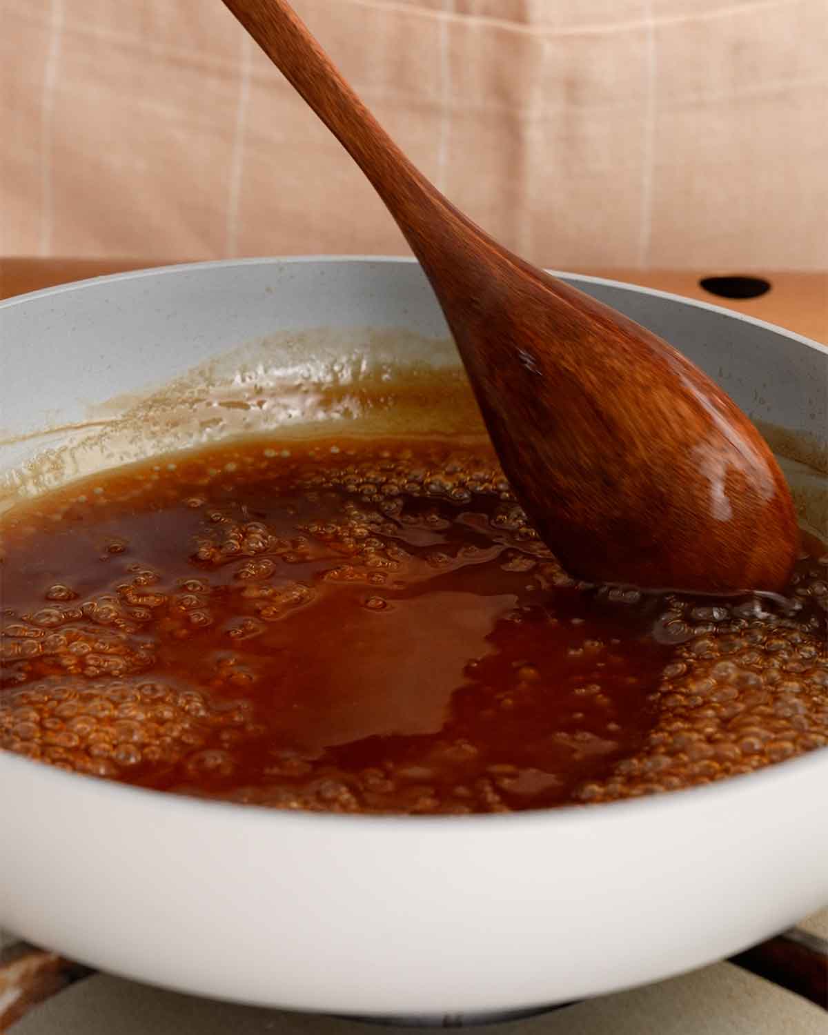 A small sauce pan containing glossy brown sauce and a wooden spoon is stirring the sauce.