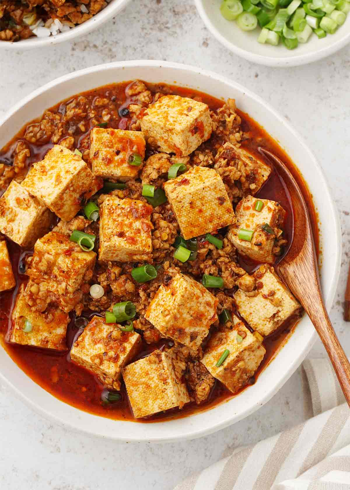 A white bowl containing tofu cubes with minced meat and red spicy mapo sauce.